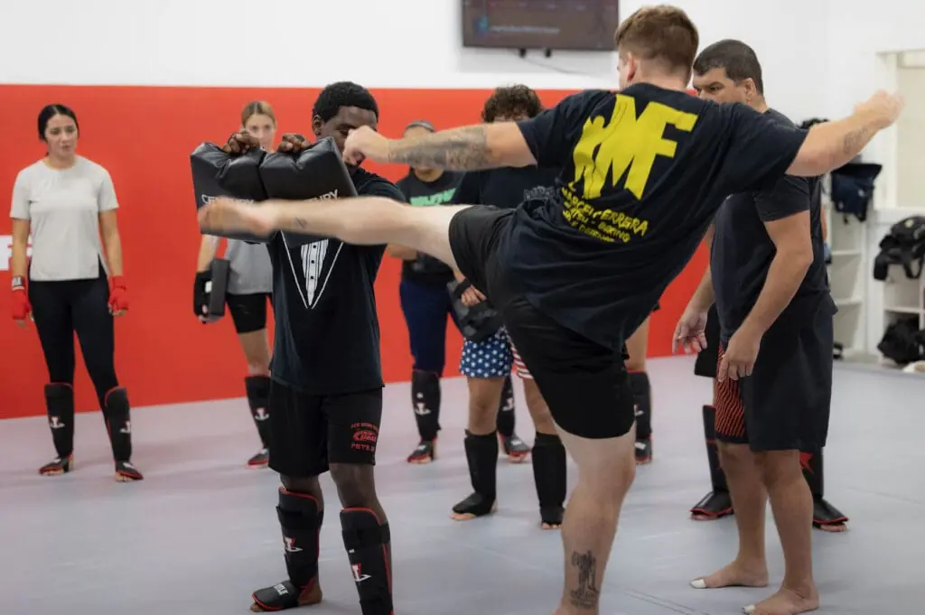 Student driving a body kick into the focus pads during a Muay Thai class at American Top Team Winter Garden